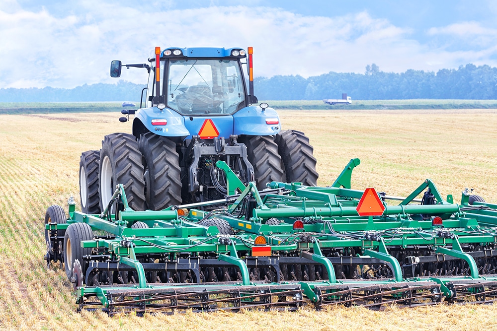 An agricultural tractor with a hitch, harrow, stands against the background of a harvested wheat field