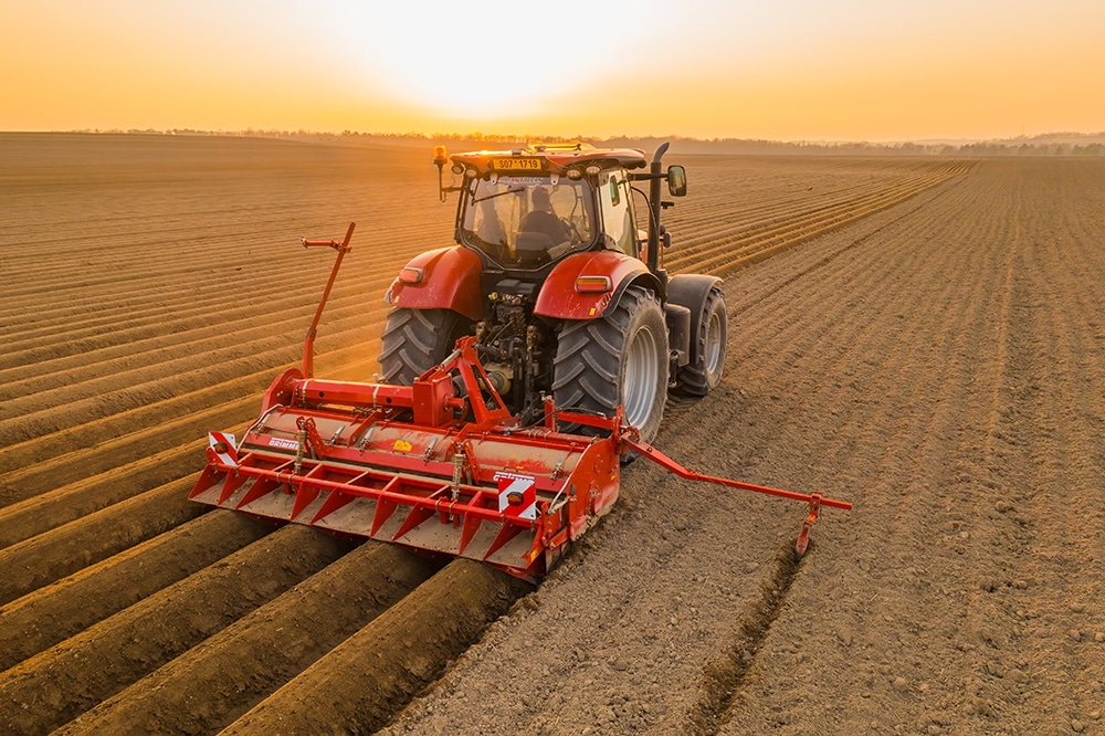 PRAGUE , CZECH REPUBLIC - MARCH 18 2022: Heavy tractor harrows in field dragging plow on purified soil. Contemporary agricultural transportation works at bright sunset in countryside